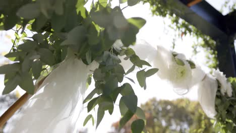 Nahaufnahme-Eines-Hochzeitsbogens-Mit-Dekorationen-Und-Blumen-Im-Sonnigen-Garten,-In-Zeitlupe