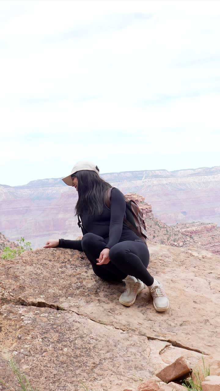 Giovane donna seduta su una sporgenza rocciosa con vista sul Grand Canyon