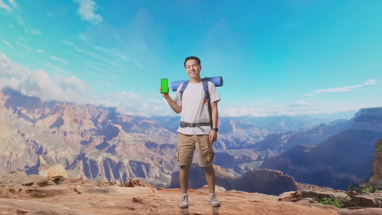 Full Body Of Asian Male Hiker With Mountaineering Backpack Smiling And Showing Mock Up Green Screen Smartphone While Traveling At The Top Of Mountain