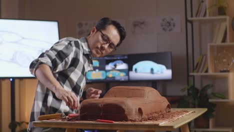 asian man automotive designer walking into the studio to sit down and work on the sculpture of car clay