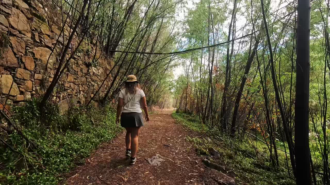 A girl hikes along a trail in the woods near the Mondego River in Portugal, surrounded by lush trees and natural scenery