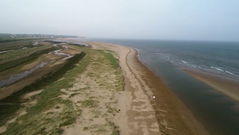 disparo de dron descendente que revela a un hombre corriendo a lo largo de la costa de norfolk con olas golpeando la orilla y mirando hacia hunstanton