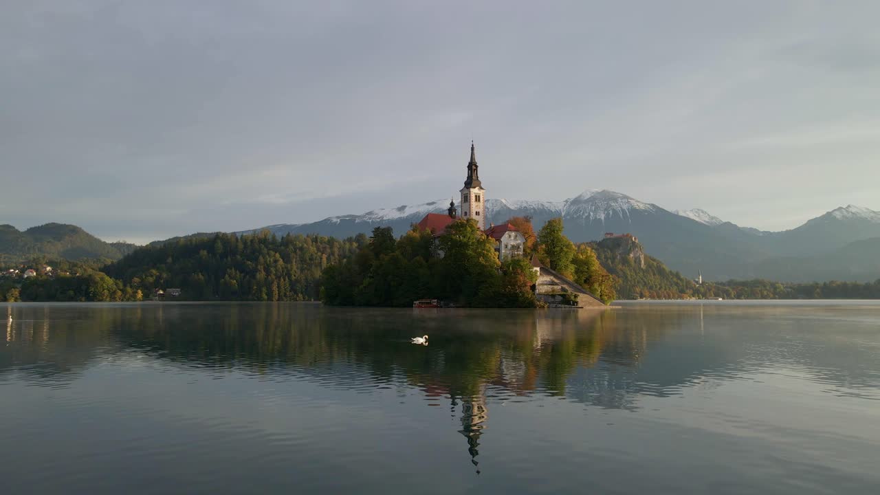 Chiesa sull'isola del Lago di Bled riflessa in acque tranquille con montagne innevate