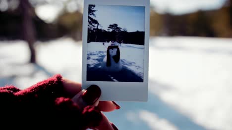 mujer sosteniendo una foto polaroid de un hombre de nieve en un bosque de montaña nevado