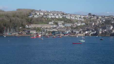 gig boat crew rowing along fowey river with cornish polruan fishing village in background - wide shot