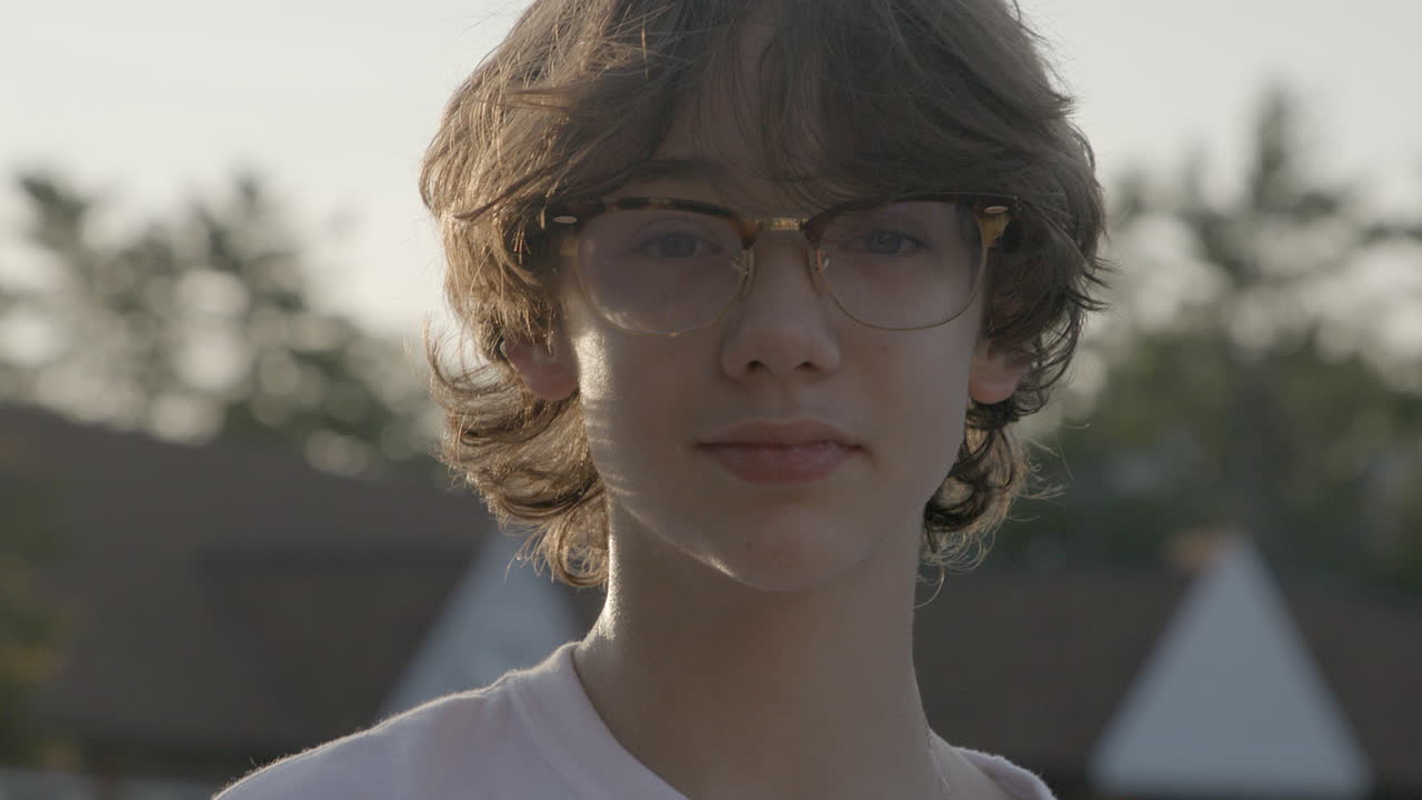 Portrait of an attractive teenage boy with glasses looking into camera with confidence outside at golden hour