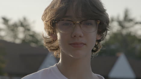 Portrait-of-an-attractive-teenage-boy-with-glasses-looking-into-camera-with-confidence-outside-at-golden-hour