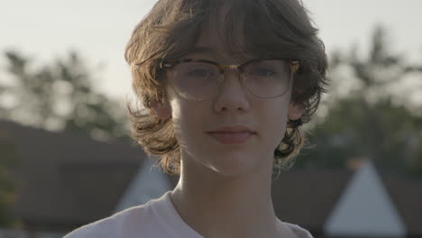 portrait of an attractive teenage boy with glasses looking into camera with confidence outside at golden hour