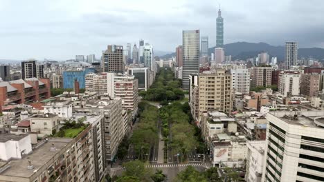 Vuelo-Aéreo-Sobre-La-Avenida-Verde-Renai-En-La-Ciudad-De-Taipei-Con-La-Famosa-Torre-101-En-El-Fondo,-Taiwán