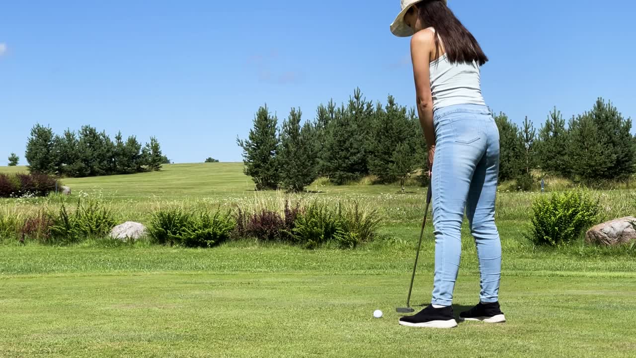 golfista femenina usa un palo de putter para golpear la pelota en la copa, campo verde en letonia