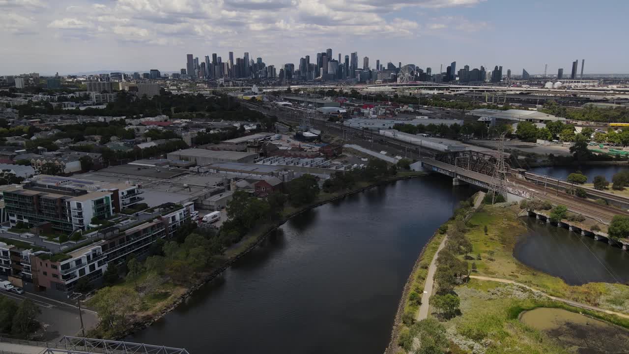 Aerial drone over Maribyrnong river, moving towards Melbourne skyline above rail tracks