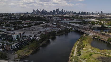 aerial drone over maribyrnong river, moving towards melbourne skyline above rail tracks