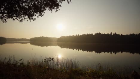 sunrise time lapse of a lake in ontario cottage country with the silhouette of trees and reflection on the lake, while clouds roll past in the summer. canada