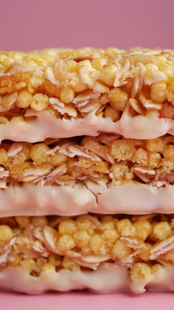 Barrette di granola impilate con rivestimento bianco su sfondo rosa