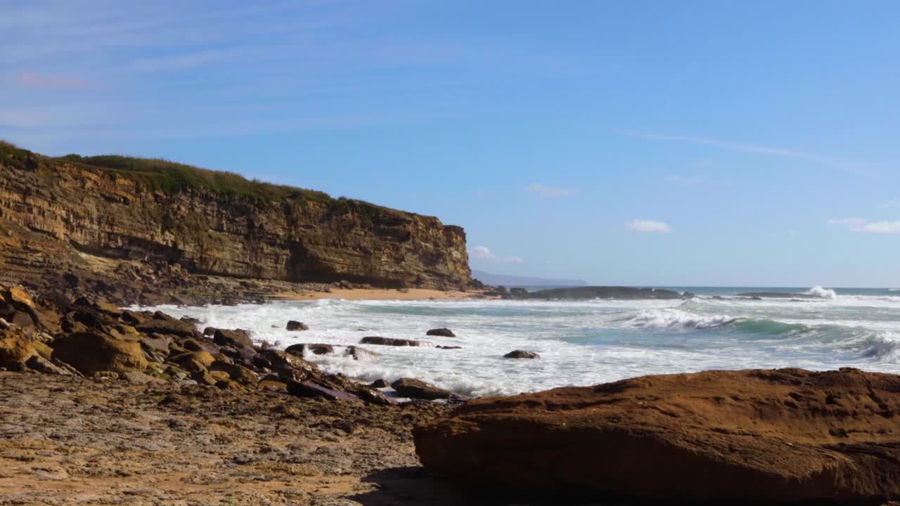 Ocean meeting a cliff with waves hitting the rocks on a sunny day
