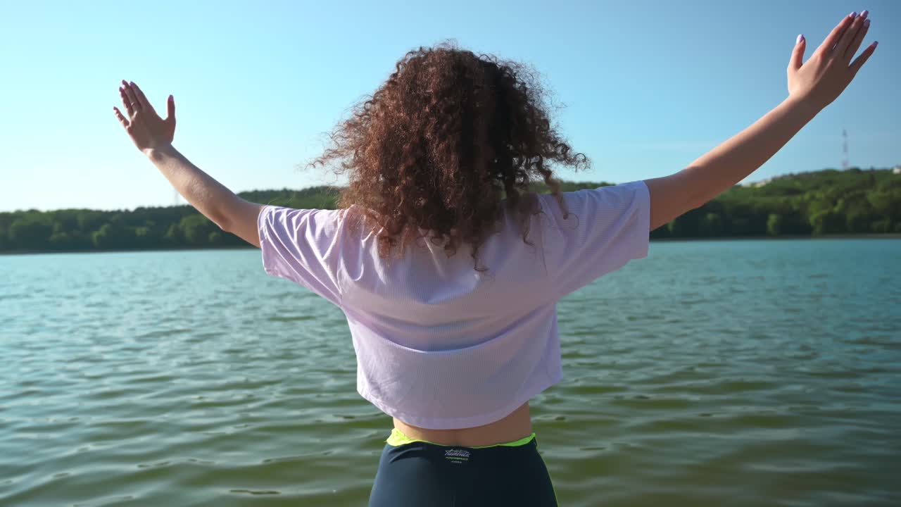 Young curly woman practicing yoga near the lake while wearing black protective mask. Sunny day. Corona Virus idea. Chisinau, Moldova