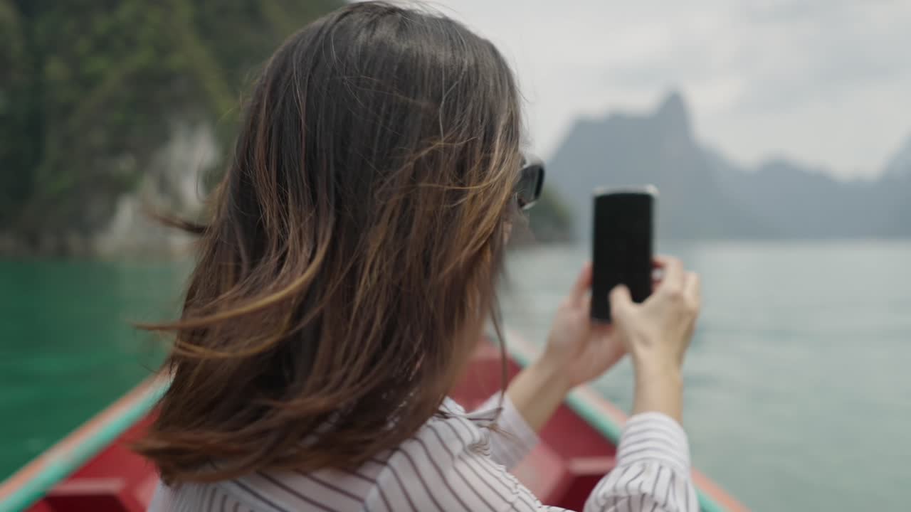 Woman in boat taking photo of scenic lake and mountains