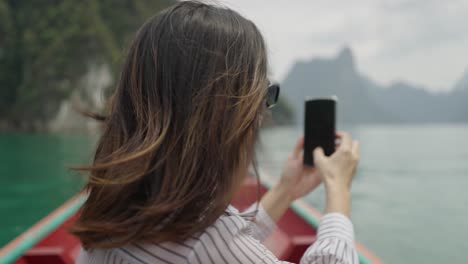 woman in boat taking photo of scenic lake and mountains