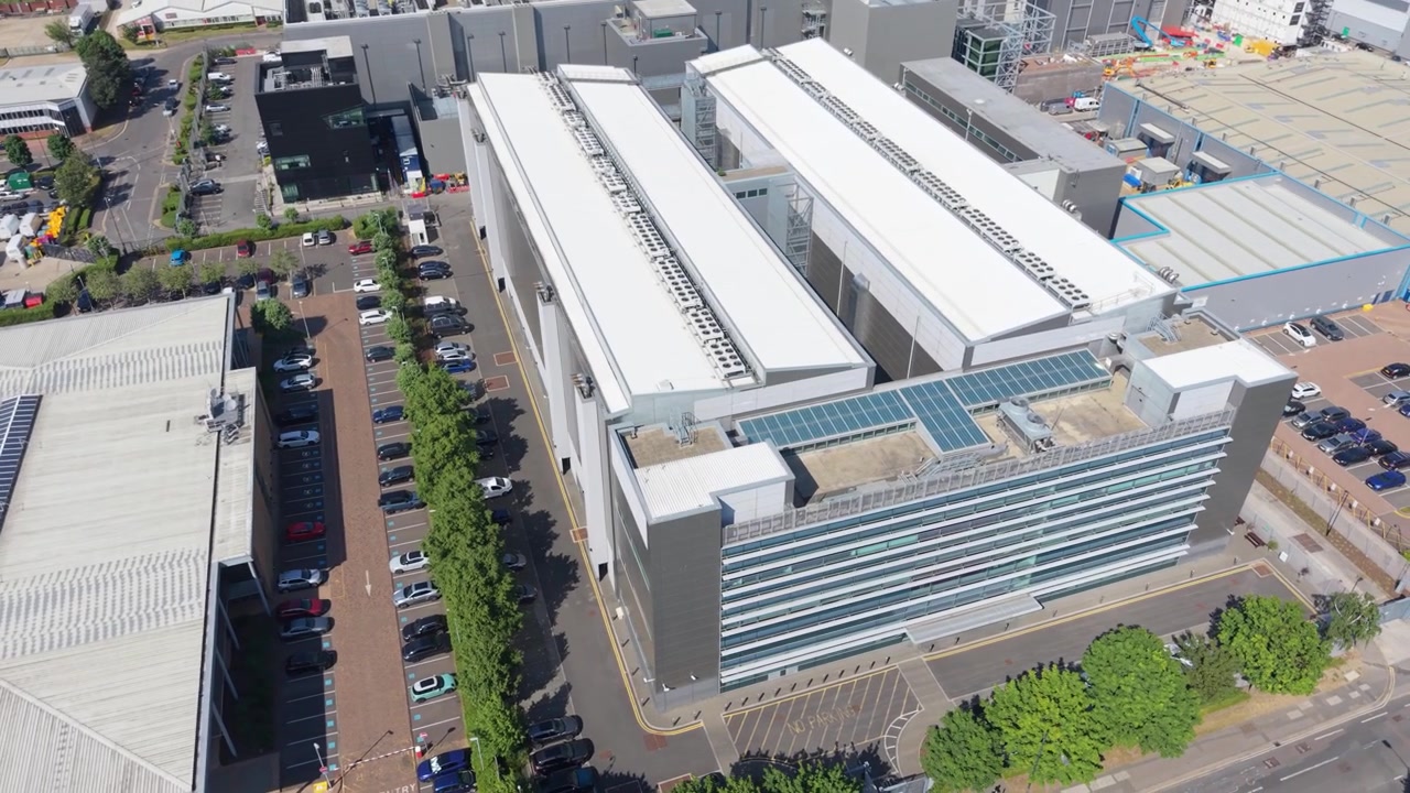 Panoramic aerial view of a large modern data center facility. Multiple buildings with white roofs and glass facades are visible.