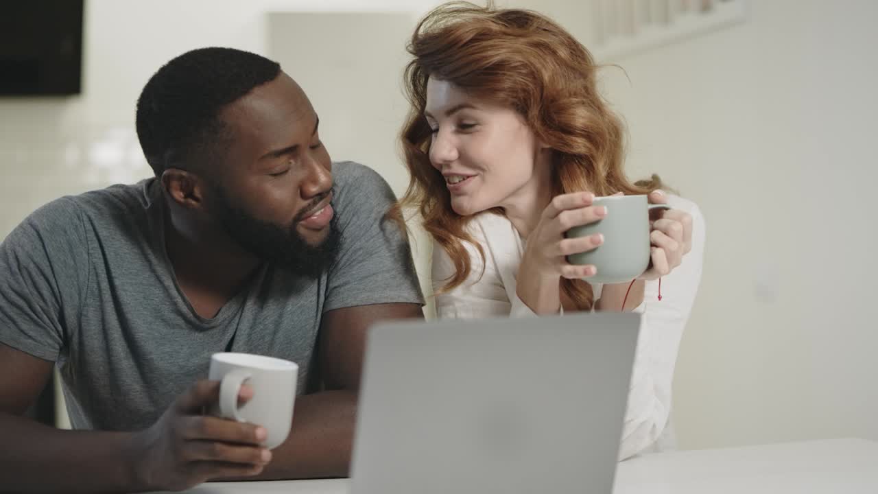 una pareja feliz hablando en una cocina abierta. un hombre y una mujer sonrientes mirando la computadora portátil.
