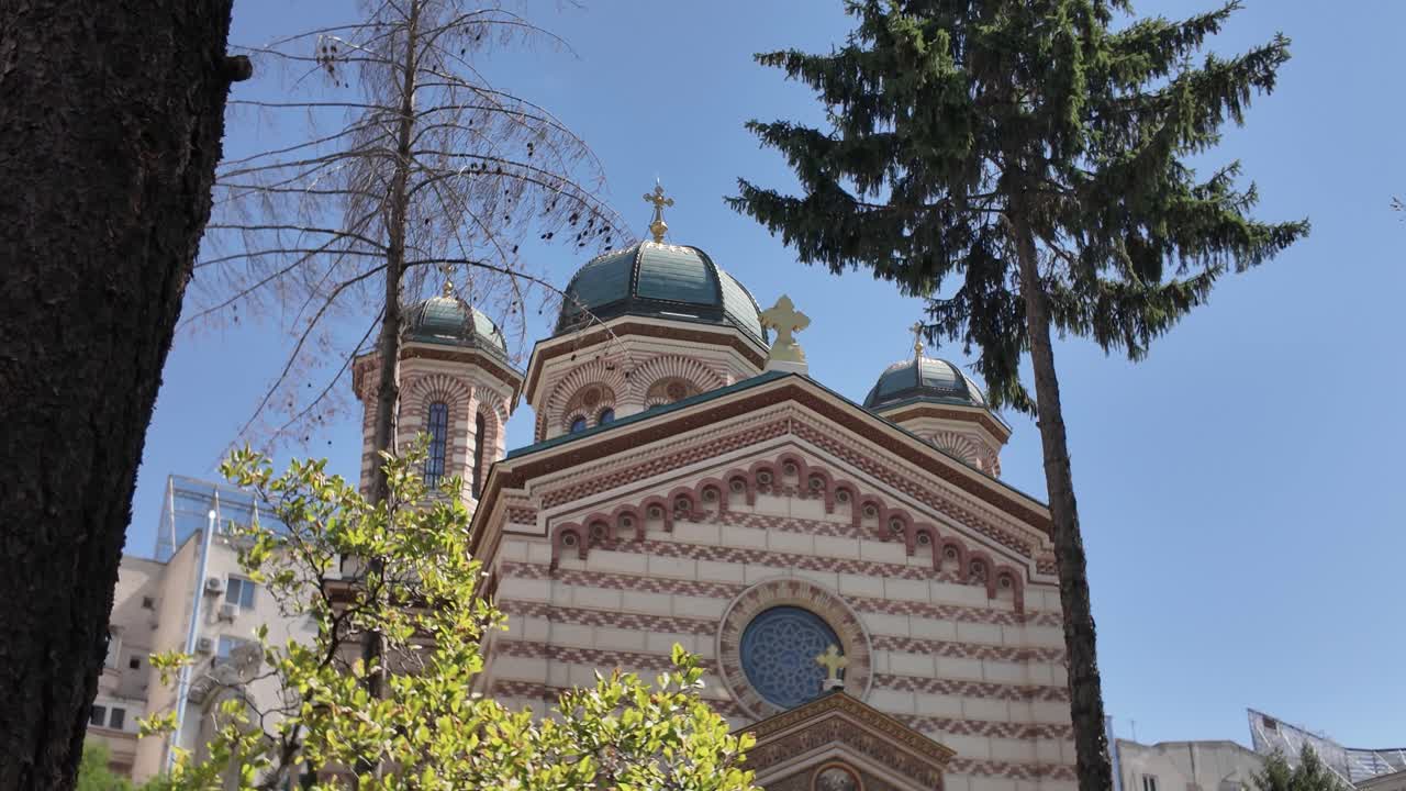 Chiesa di Domnița Bălașa a Bucarest, inquadrata da alberi in primo piano, che unisce l'architettura religiosa con elementi naturali