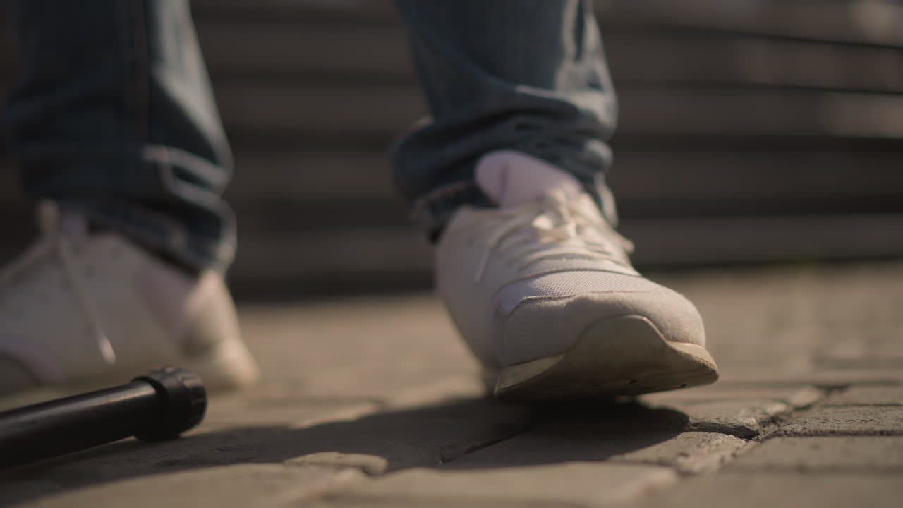 closeup light sneaker on pavement near microphone stand busker foot taps rhythm against cobblestone under warm sunset light, jeans cuff visible, urban stair background, intimate motion and groove
