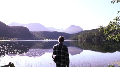 man standing at a beautiful lake, thinking, enjoying and relaxing after a long hike, breathing in life, slow motion shot in norway, europe