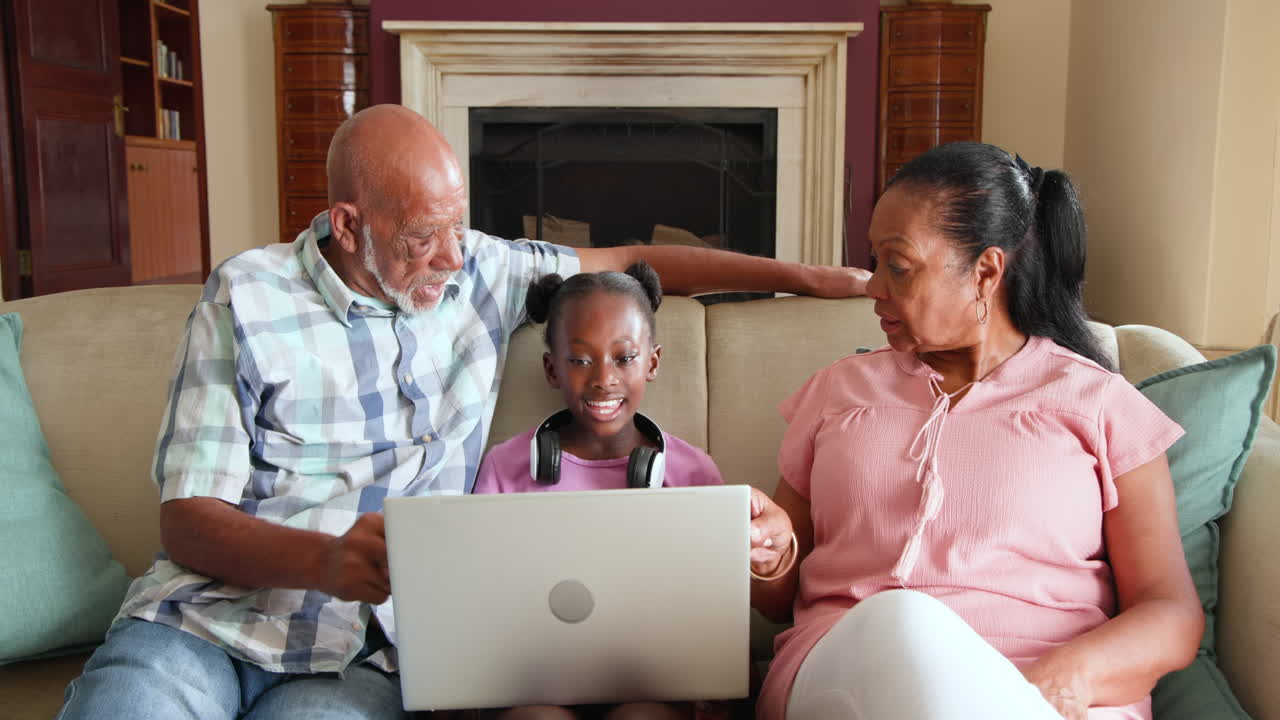 Diverse grandparents and granddaughter using laptop together on couch, sharing moment, at home