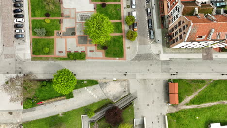 Direct-overhead-aerial-view-of-a-landscaped-public-square-in-Elbląg,-with-lush-green-trees,-walkways,-benches,-and-surrounding-street-with-parked-cars