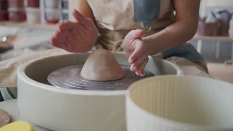 female potter shapes piece of clay on the pottery wheel.