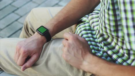 hombre con un reloj inteligente con una pantalla verde, camisa a cuadros y pantalones caqui ligeros