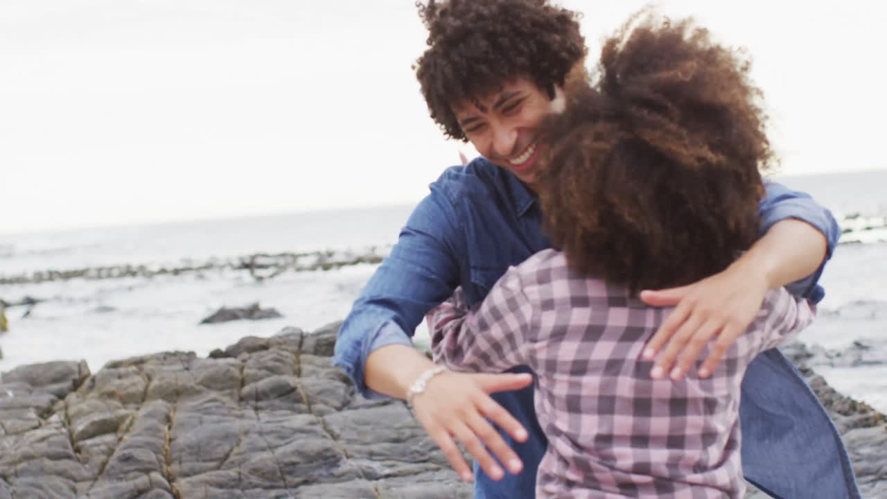 pareja afroamericana abrazándose en las rocas cerca del mar