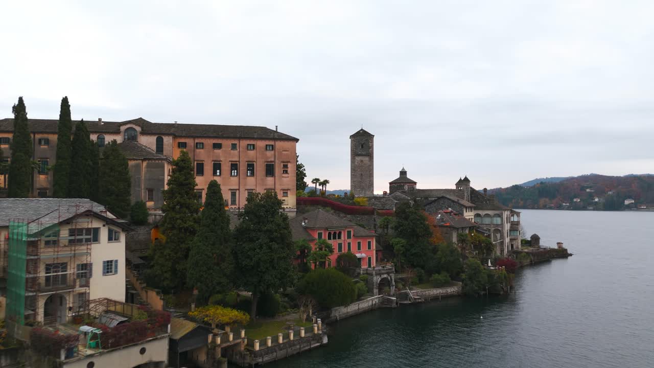 Cinematic drone view of the historic Benedictine monastery and Basilica on Isola San Giulio. Aerial shot of the island in Lake Orta with calm water, Italy