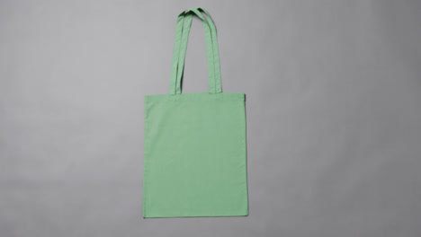 Primer-Plano-De-Una-Bolsa-Verde-Sobre-Fondo-Gris,-Con-Espacio-Para-Copiar,-Cámara-Lenta