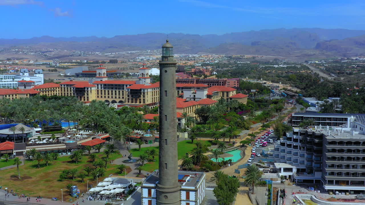 Beautiful aerial view of Gran Canaria lighthouse, flying near big tower, seaside tower. Rotating aerial view of tourist town and lighthouse with mountains in the distance
