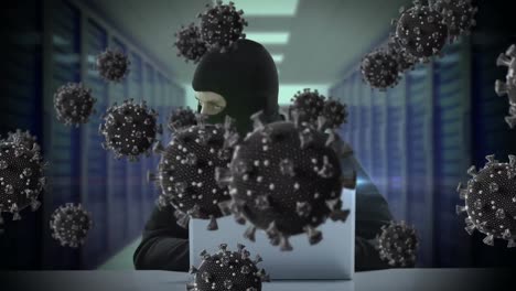 Animation-of-of-macro-covid19-cells-over-man-wearing-balaclava,-using-a-laptop