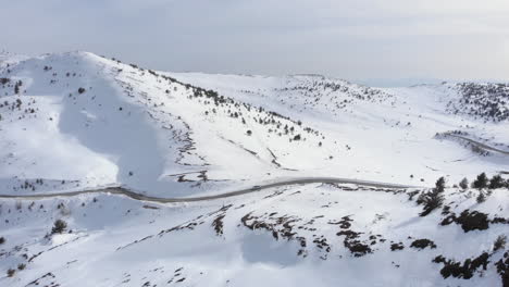 Aerial-view-of-car-passing-crossing-high-altitude-mountain-road-beautiful-slopes-covered-in-snow-winter-day