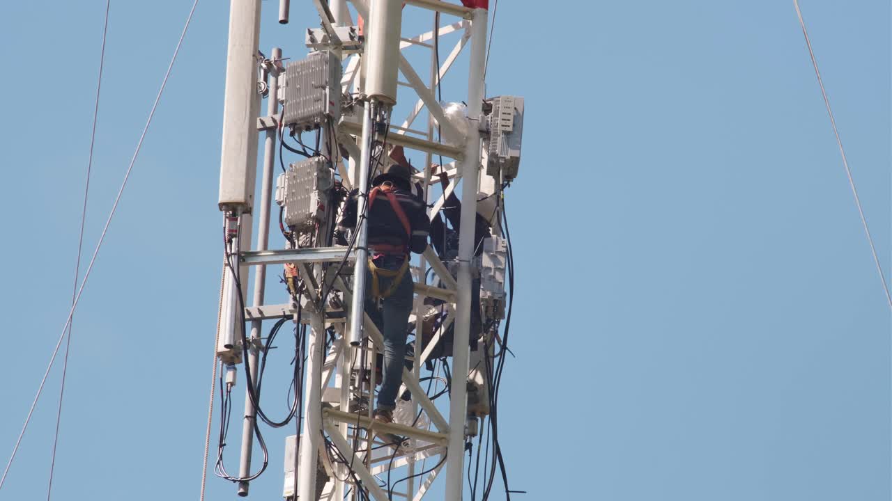 primer plano de dos hombres trabajando en una torre de comunicación y realizando reparaciones o mantenimiento