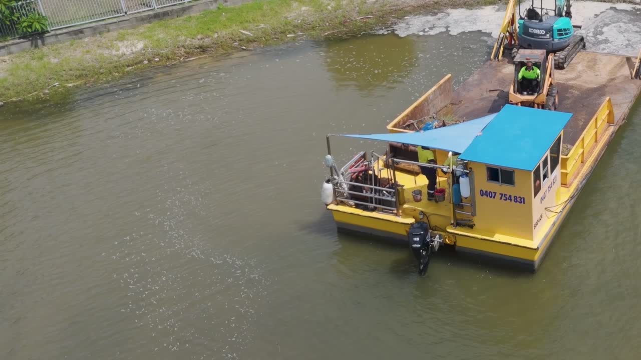 Aerial view of a barge with machinery operating in a canal near luxury homes in Broadbeach Waters, Queensland