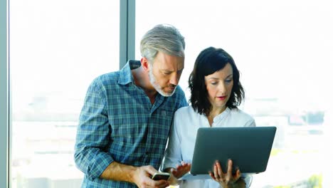 ejecutivos masculinos y femeninos usando computadora portátil cerca de la ventana