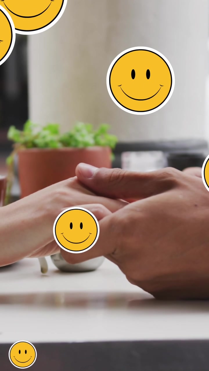 Animaatio digitaalisista emoji-kuvakkeista leijumassa valkoihoisen pariskunnan yllä, jotka ovat käsi kädessä.
