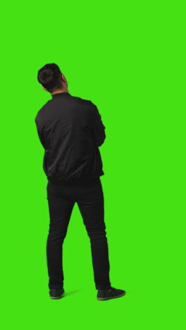 Vertical-Video-Rear-Full-Length-Portrait-Shot-Of-Bored-Or-Fed-Up-Man-Standing-And-Waiting-Against-Green-Screen