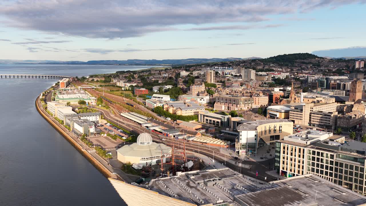 Drone pans above Dundee waterfront, highlighting modern architecture, river, and cityscape in soft morning light