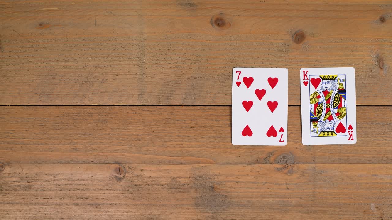 A person laying out a flush with hearts on a wooden table to educate the viewer on how to play poker
