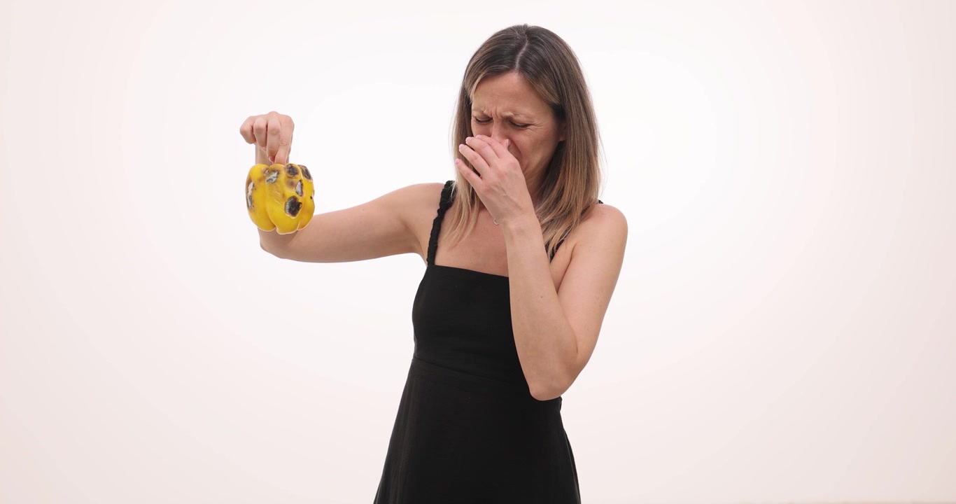 Woman holds moldy yellow bell pepper with disgusted expression