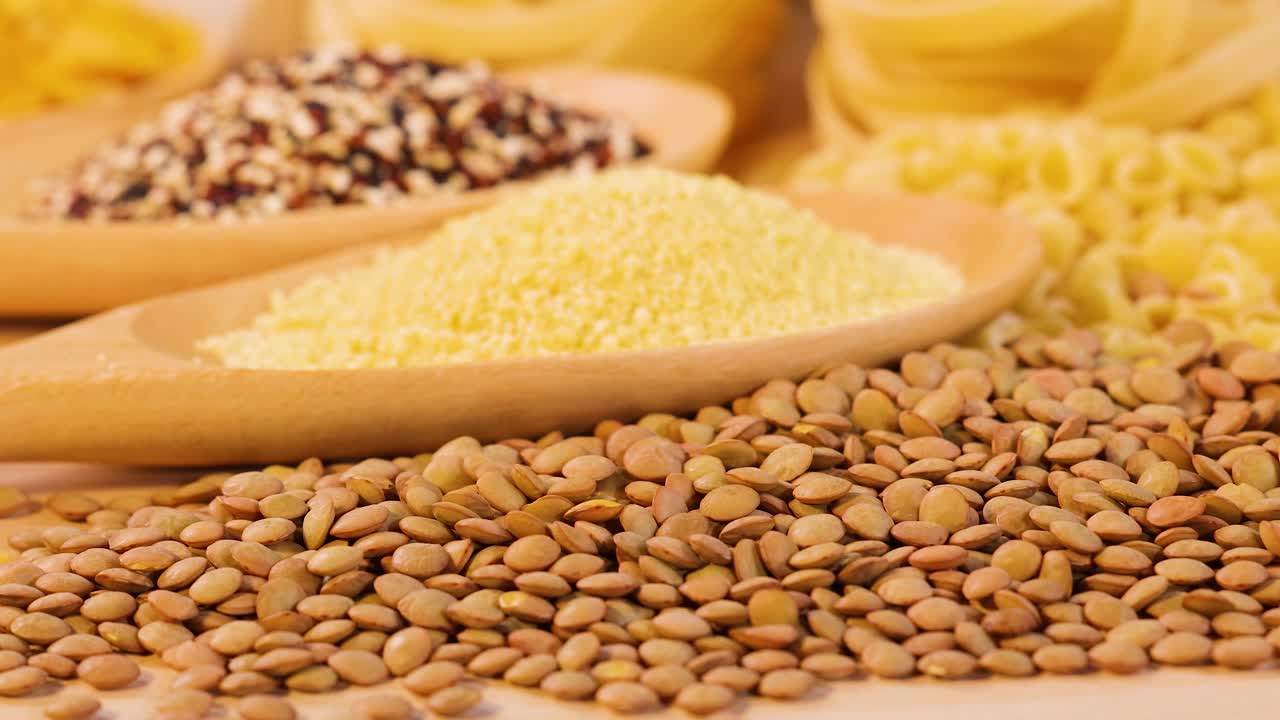 Close-up of quinoa, lentils, and couscous in warm lighting. Wooden spoon and natural textures create a rustic culinary scene