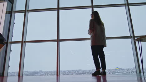 long-haired lady in suit walks near the panoramic windows. young woman looks at the city panorama. low angle view.