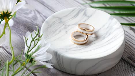 elegantes anillos dorados y blancos en un plato de mármol con flores