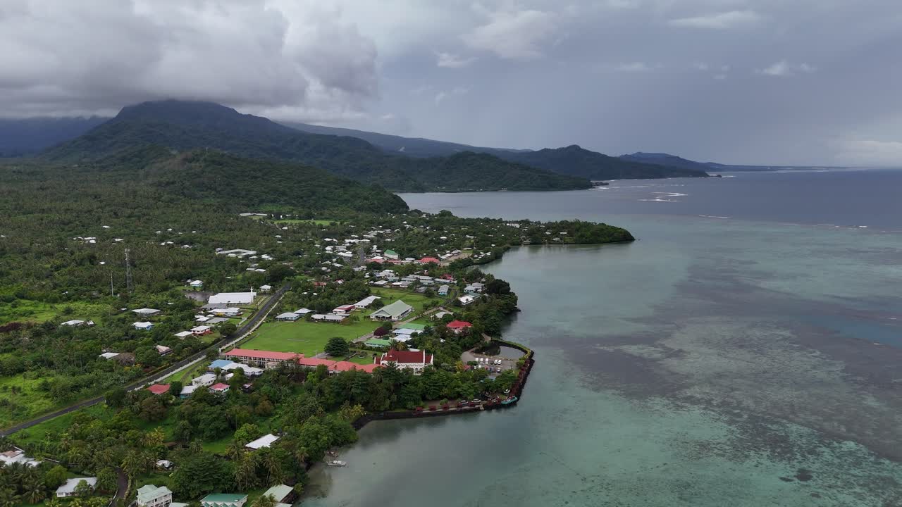 Vista aerea da drone di un villaggio costiero su una lussureggiante isola tropicale delle Samoa. Paesaggi verdeggianti e montagne vulcaniche incontrano le acque blu del Pacifico meridionale.