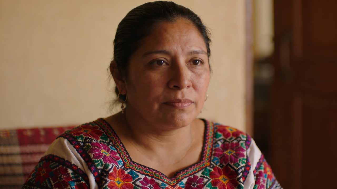 Listening middle-aged Hispanic woman shifting gaze and blinking at home, wearing embroidered blouse